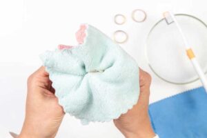 Hands gently polishing a gold-filled ring with a soft cleaning cloth, with additional cleaning tools and rings in the background.