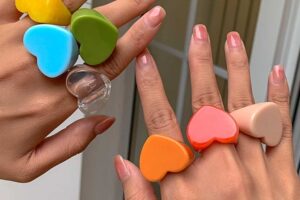 Close-up of hands wearing colorful heart-shaped acrylic rings in vibrant hues including orange, blue, green, and yellow.
