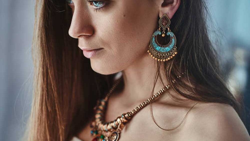Close-up of a woman wearing bohemian-style jewelry, featuring vibrant turquoise statement earrings and a layered necklace with colorful accents.