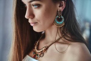 Close-up of a woman wearing bohemian-style jewelry, featuring vibrant turquoise statement earrings and a layered necklace with colorful accents.