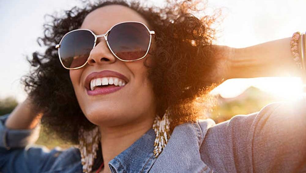 Woman wearing statement earrings and sunglasses with a denim jacket in the sunlight, showcasing modern jewelry trends.