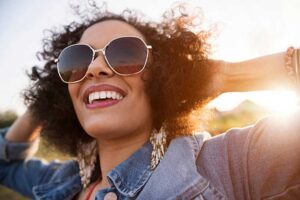 Woman wearing statement earrings and sunglasses with a denim jacket in the sunlight, showcasing modern jewelry trends.