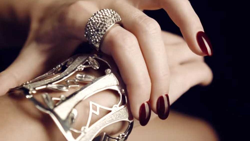 Close-up of a woman's hand wearing an intricate silver cuff bracelet and a sparkling ring, paired with dark red polished nails, showcasing an elegant jewelry look.