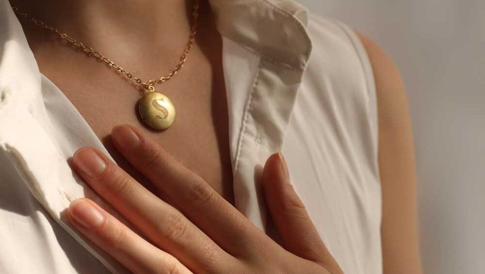 Close-up of a woman wearing a gold locket necklace with her hand gently touching it, symbolizing sentimental value.
