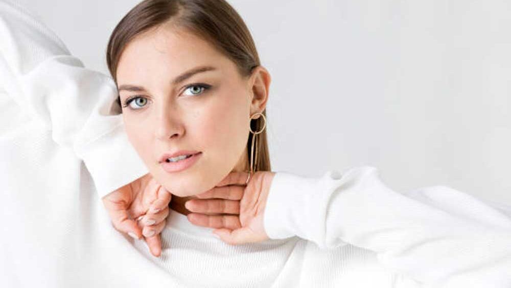 A woman showcasing a minimalist jewelry look, wearing sleek gold hoop earrings paired with a white outfit for an elegant and refined style.