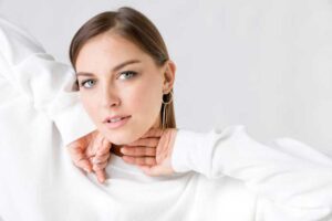 A woman showcasing a minimalist jewelry look, wearing sleek gold hoop earrings paired with a white outfit for an elegant and refined style.