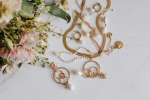 A stylish arrangement of mix-and-match jewelry pieces, featuring gold necklaces, rings, and earrings alongside delicate flowers on a white marble surface.
