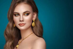 Elegant woman wearing gold textured earrings and a matching textured pendant necklace against a teal background.