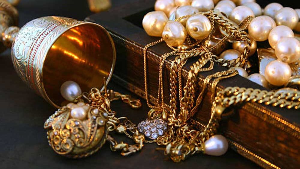 A collection of gold heirloom jewelry and pearls spilling out of a vintage wooden box, symbolizing timeless elegance and family heritage.
