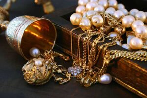 A collection of gold heirloom jewelry and pearls spilling out of a vintage wooden box, symbolizing timeless elegance and family heritage.