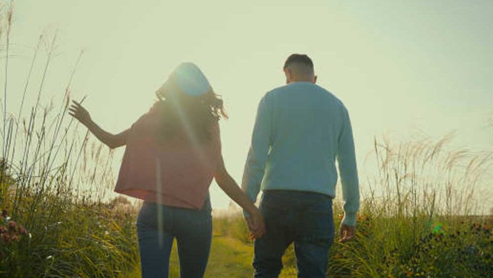 A couple walking hand in hand through a sunlit field, symbolizing love, trust, and new beginnings.