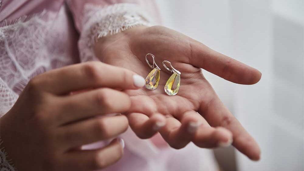 Close-up of a person gently holding a pair of teardrop earrings with yellow gemstones.