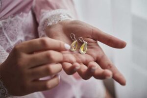 Close-up of a person gently holding a pair of teardrop earrings with yellow gemstones.