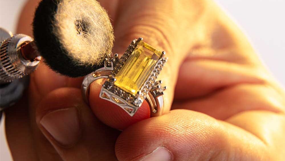 Close-up of a person polishing a yellow gemstone ring with a rotary tool for cleaning and maintenance.