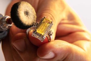Close-up of a person polishing a yellow gemstone ring with a rotary tool for cleaning and maintenance.