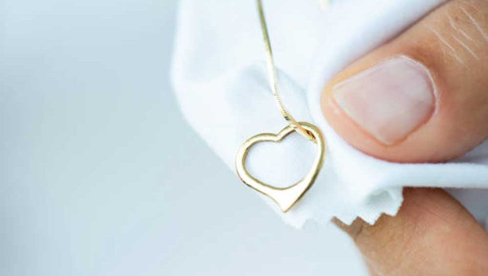 Close-up of a person polishing a gold heart-shaped necklace with a soft white cleaning cloth.