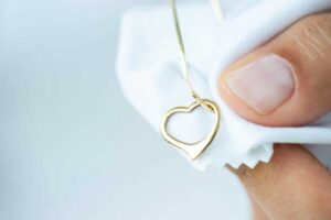Close-up of a person polishing a gold heart-shaped necklace with a soft white cleaning cloth.