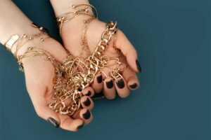 Close-up of hands holding a collection of gold-plated chains and bracelets against a teal background.