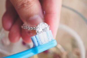 Close-up of a diamond ring being gently cleaned with a toothbrush, showing the process of jewelry care.