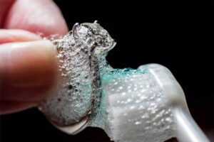Close-up of a silver ring being cleaned with a toothbrush and soapy bubbles.