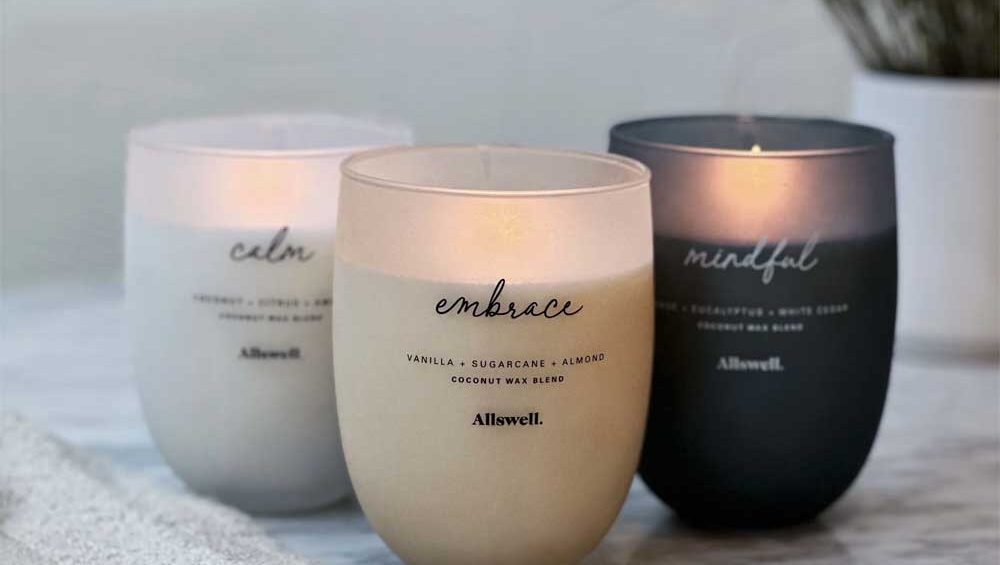 A set of three Allswell candles labeled "Embrace," "Mindful," and "Calm," placed on a marble surface with a soft, neutral background.
