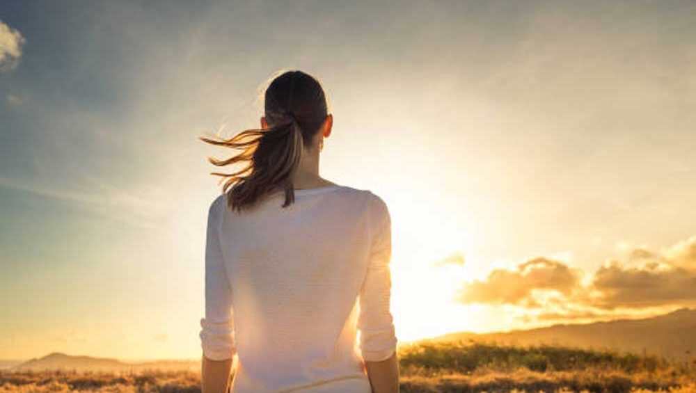 A woman standing in a peaceful field at sunrise, gazing at the horizon, symbolizing self-reflection and new beginnings.