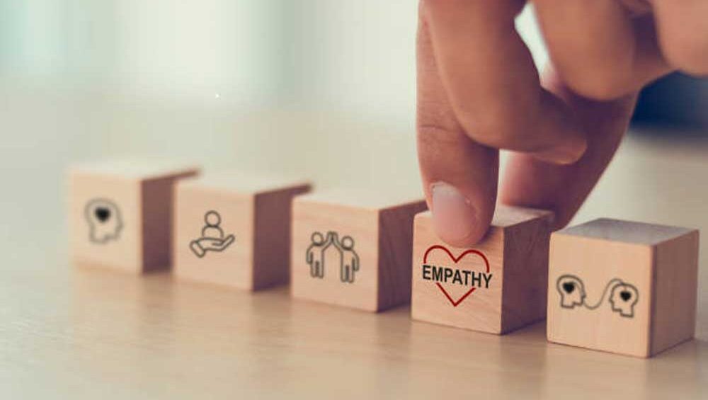 A hand selecting a wooden block with the word "Empathy" and a heart symbol, representing emotional connection and understanding.