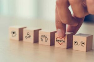 A hand selecting a wooden block with the word "Empathy" and a heart symbol, representing emotional connection and understanding.