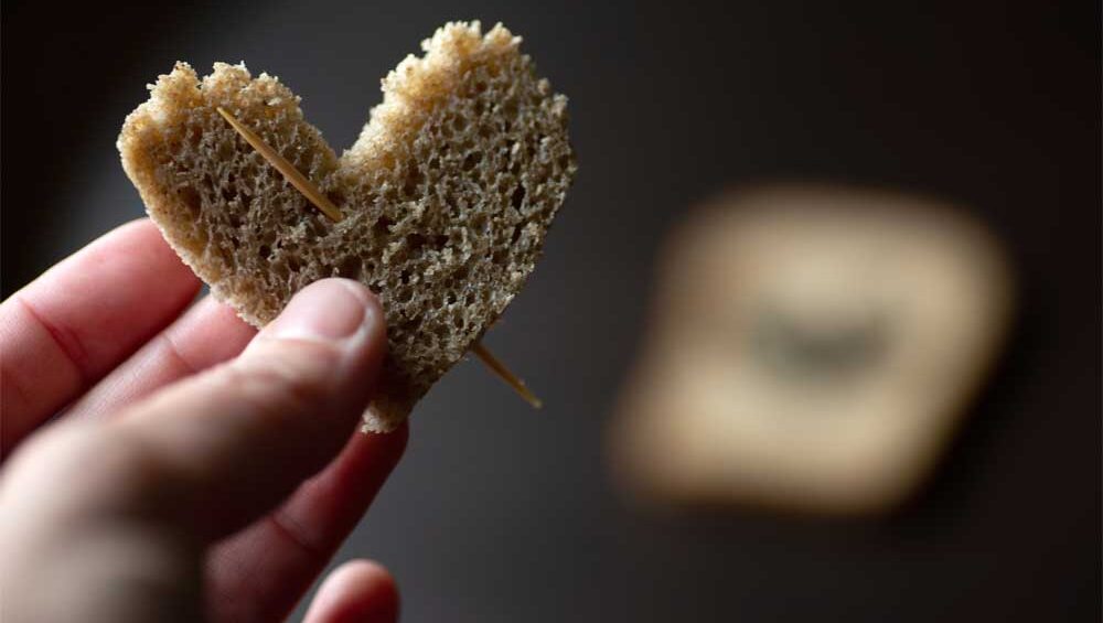 A broken heart-shaped piece of bread held together with toothpicks, symbolizing emotional breadcrumbing and almost-love.
