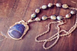 Close-up of a lapis lazuli pendant necklace with baroque pearls and a gold chain on a rustic wooden surface.