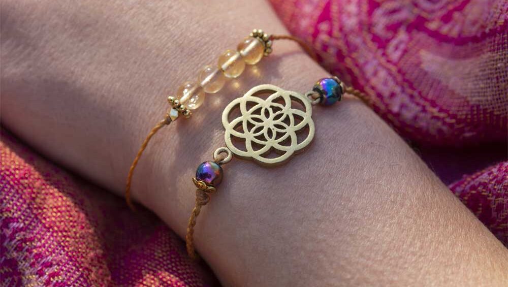 Gold Seed of Life bracelet with iridescent beads on wrist wrapped in pink paisley fabric