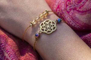 Gold Seed of Life bracelet with iridescent beads on wrist wrapped in pink paisley fabric