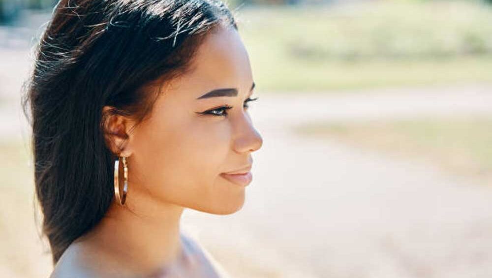 Woman wearing hoop earrings looking into sunlight, symbolizing self-reflection and inner clarity.