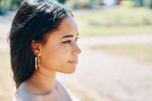 Woman wearing hoop earrings looking into sunlight, symbolizing self-reflection and inner clarity.