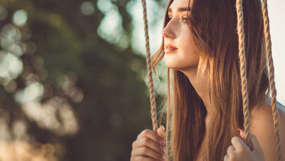 Young woman on a swing in soft golden light, gazing into the distance with quiet reflection