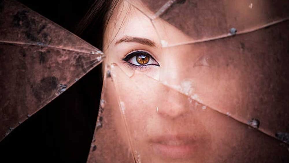 A woman's eye peers through shattered glass, symbolizing the fractured reality and emotional impact of narcissistic manipulation and self-discovery.