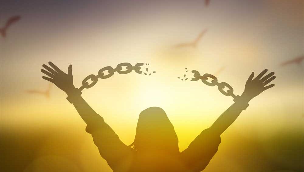 Silhouette of a woman breaking free from chains at sunrise, symbolizing freedom from trauma bonds and emotional healing.