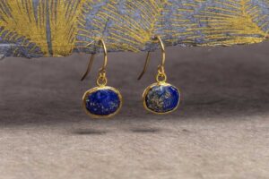 Lapis lazuli dangle earrings with gold bezel settings displayed against a textured blue and gold background