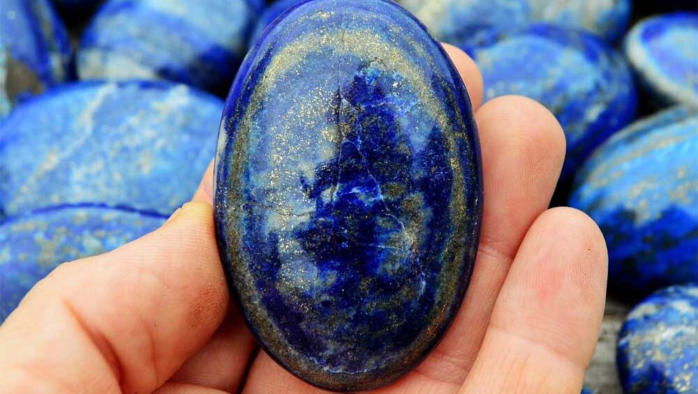 Lapis lazuli properties on display in a polished stone—deep blue color with golden pyrite flecks, held in hand for energy and healing.