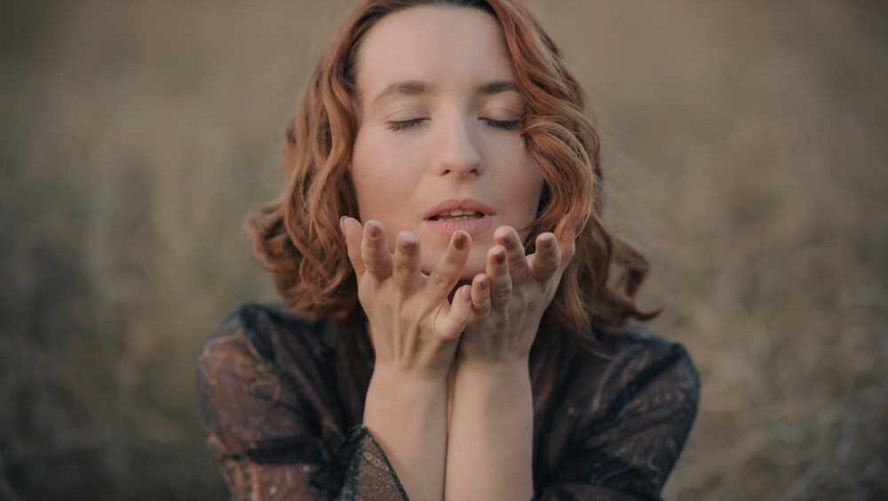 Woman embracing emotional release with closed eyes and open hands in a peaceful field