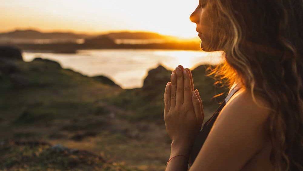 Woman standing in prayer at sunset, embracing inner healing and silent transformation.
