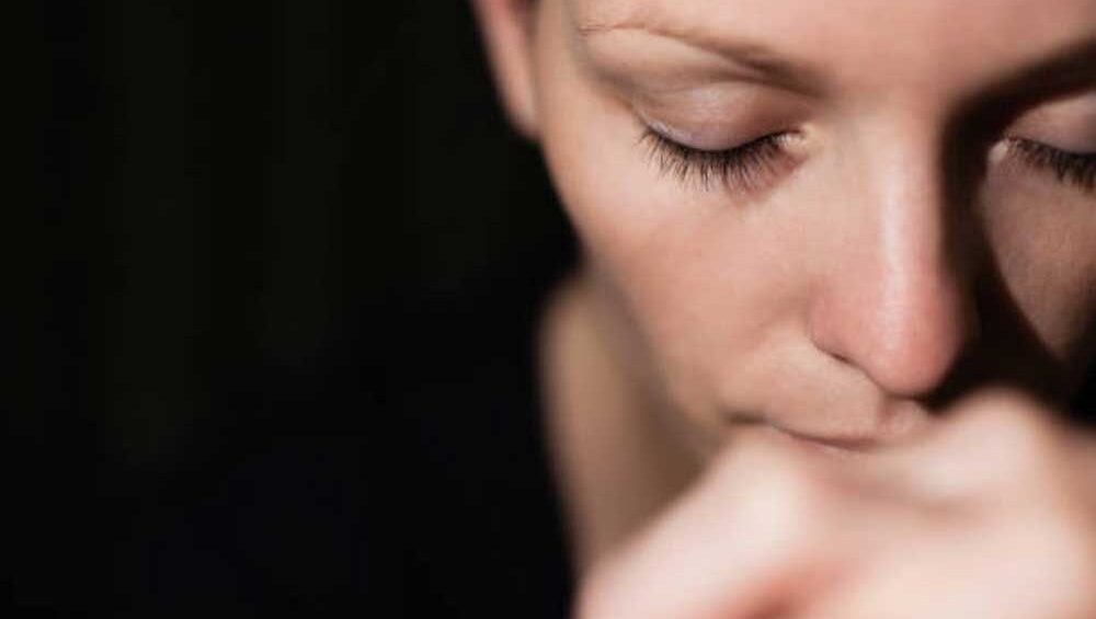 Close-up of a woman with eyes closed and hands near her face, expressing deep emotional reflection and intuitive stillness.