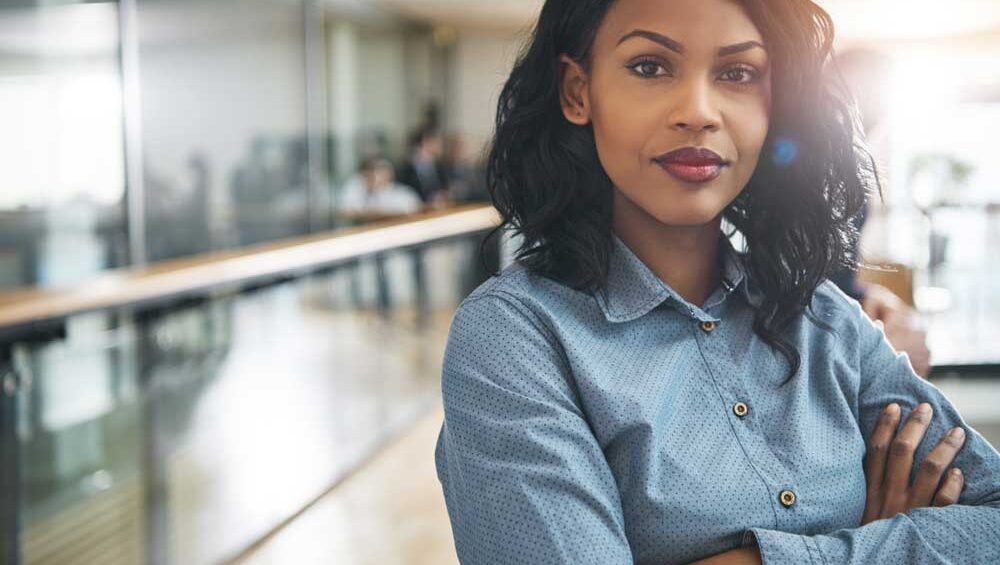 Confident woman standing with arms crossed in a bright, modern workspace, symbolizing empowerment and self-assurance.