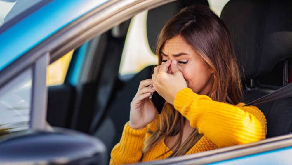 A woman sits in her car crying on the phone, visibly overwhelmed and emotional.