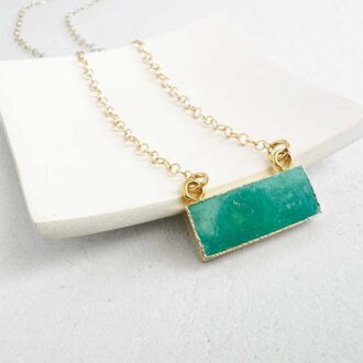 Amazonite bar necklace with raw-cut green gemstone on a 14K gold-filled chain, displayed on a white ceramic dish.