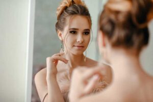 Woman in soft lighting looking at herself in the mirror while wearing delicate earrings.
