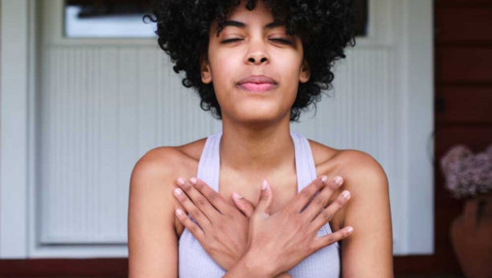 Woman sitting with eyes closed and hands crossed over her heart in a calm, grounding posture, symbolizing energetic protection and emotional healing.
