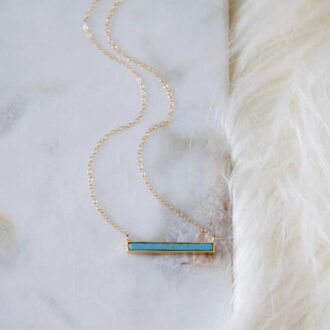 Turquoise bar necklace with 18K gold-plated pendant on a 14K gold-filled chain, displayed on a marble and fur background.