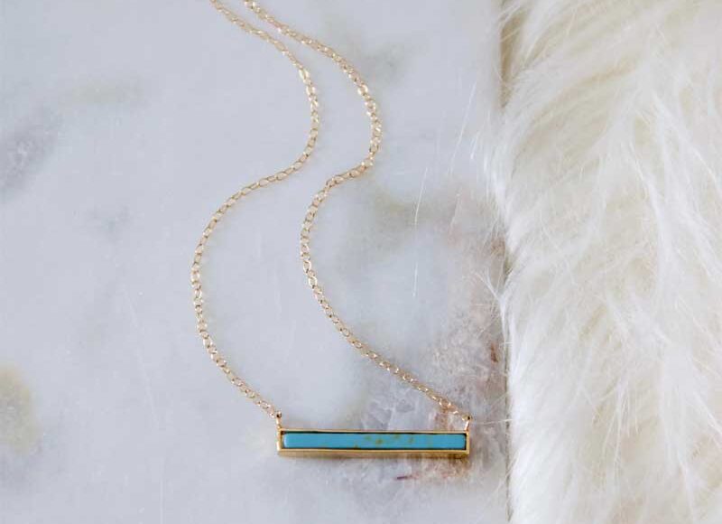 Turquoise bar necklace with 18K gold-plated pendant on a 14K gold-filled chain, displayed on a marble and fur background.
