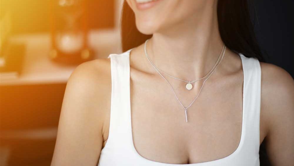 Woman wearing layered silver necklaces, including a vertical bar and a circular pendant.
